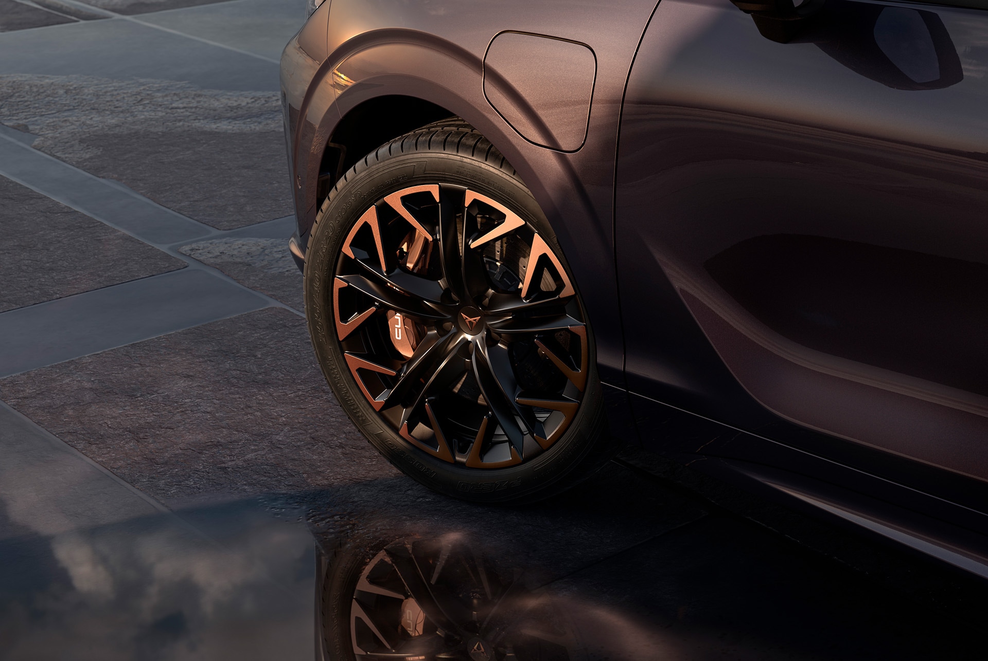 20 inch hadron copper alloy wheel on the new cupra terramar, in black with copper accents. Background includes a tiled pavement and part of the car's glossy, dark body.